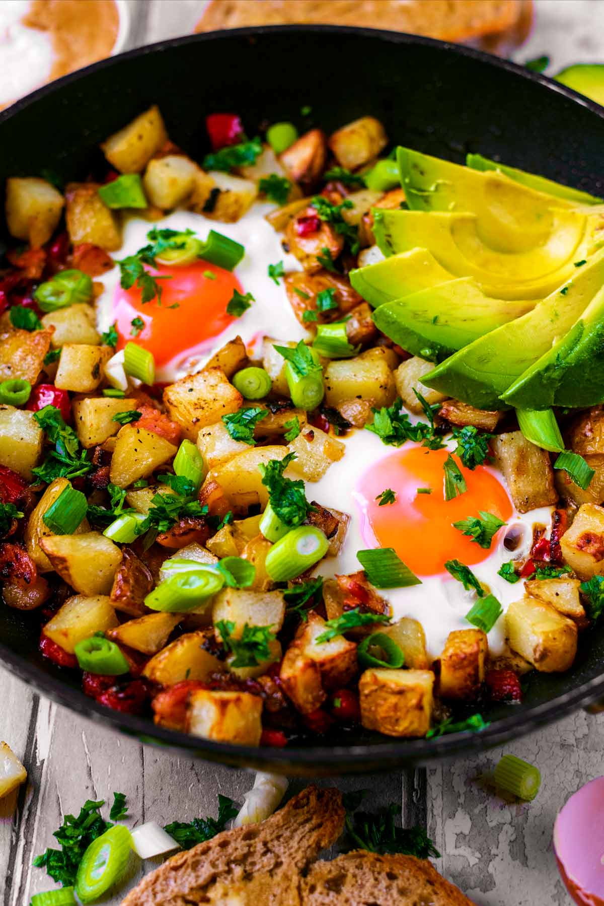 Breakfast hash in a frying pan topped with sliced avocado.