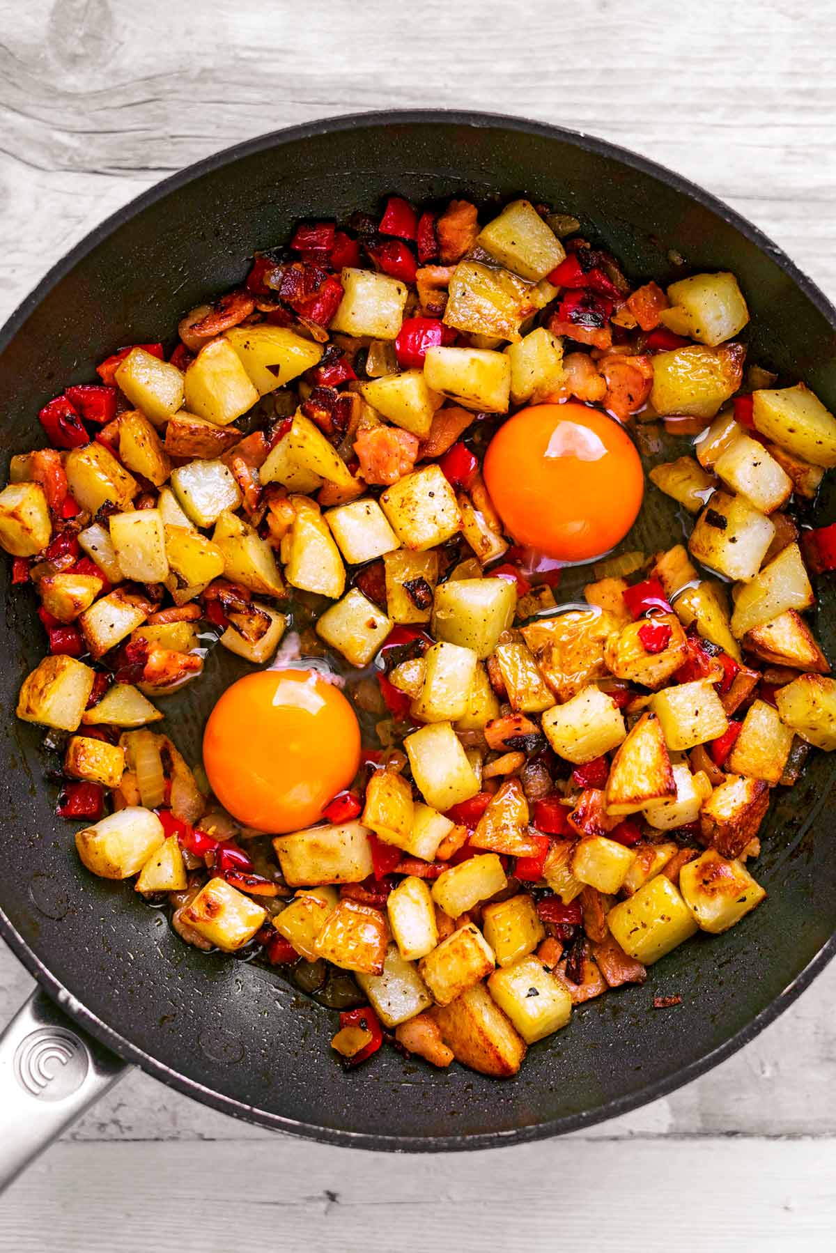 A frying pan with breakfast hash and two uncooked eggs in it.