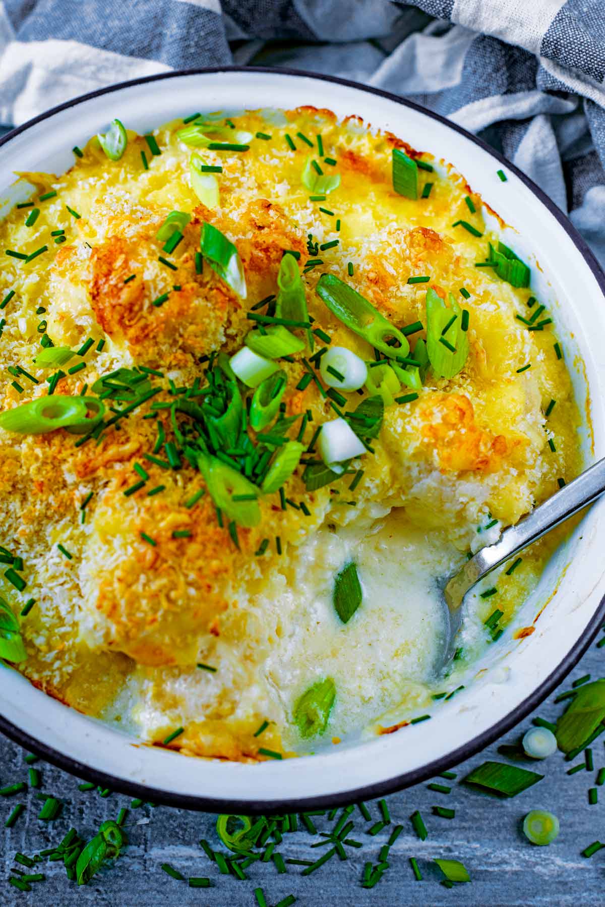 A bowl of cauliflower cheese with a spoon.