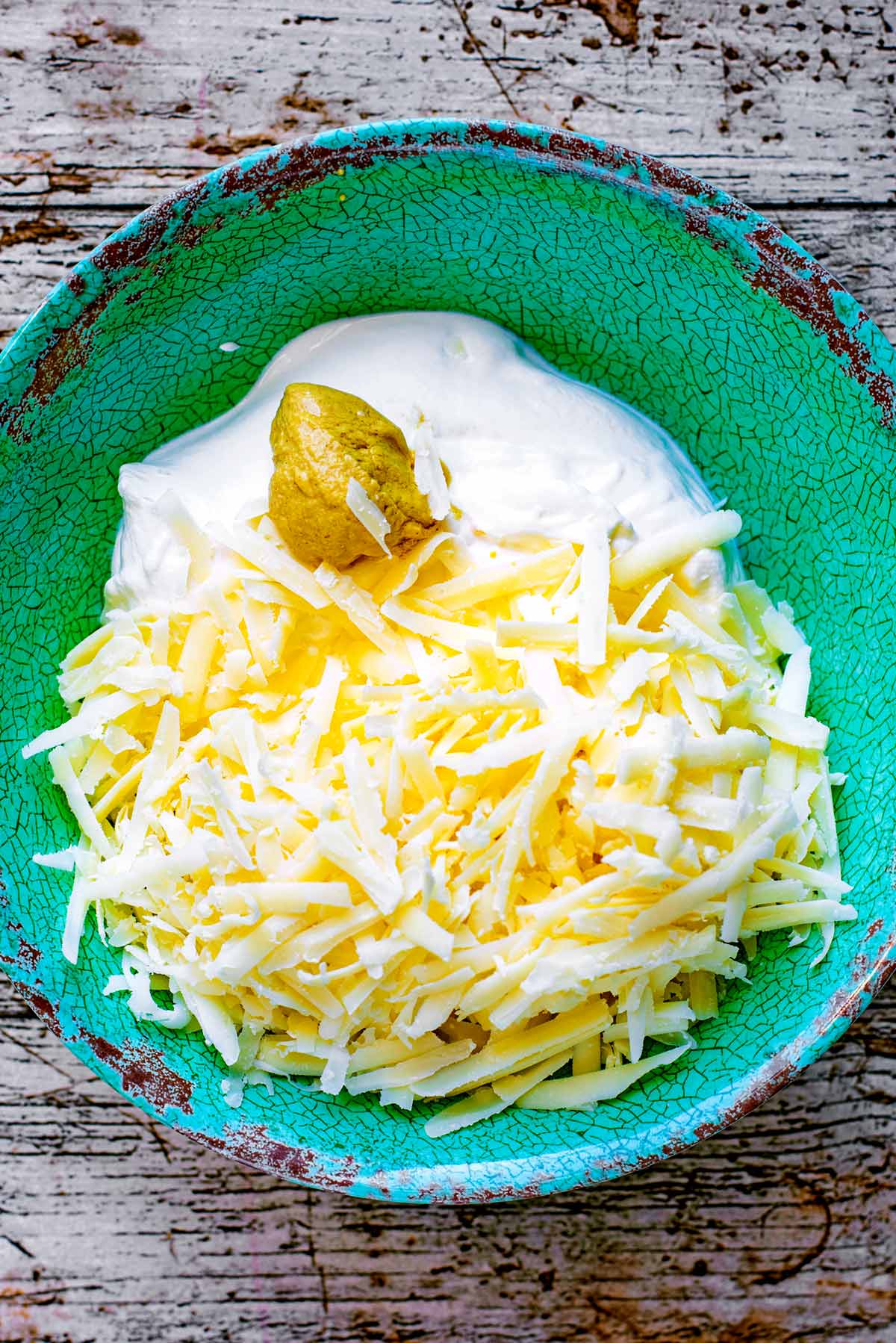 A green bowl containing grated cheese, creme fraiche and mustard.