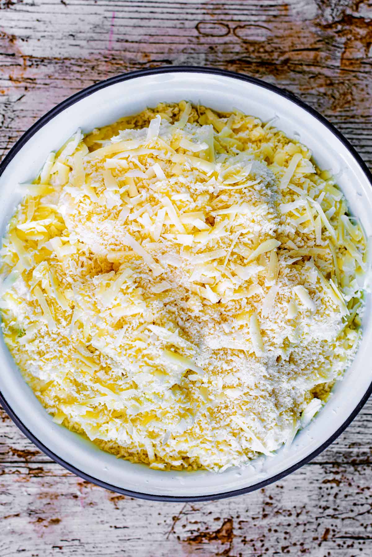 Uncooked cauliflower cheese, topped with grated cheese, in a baking dish.