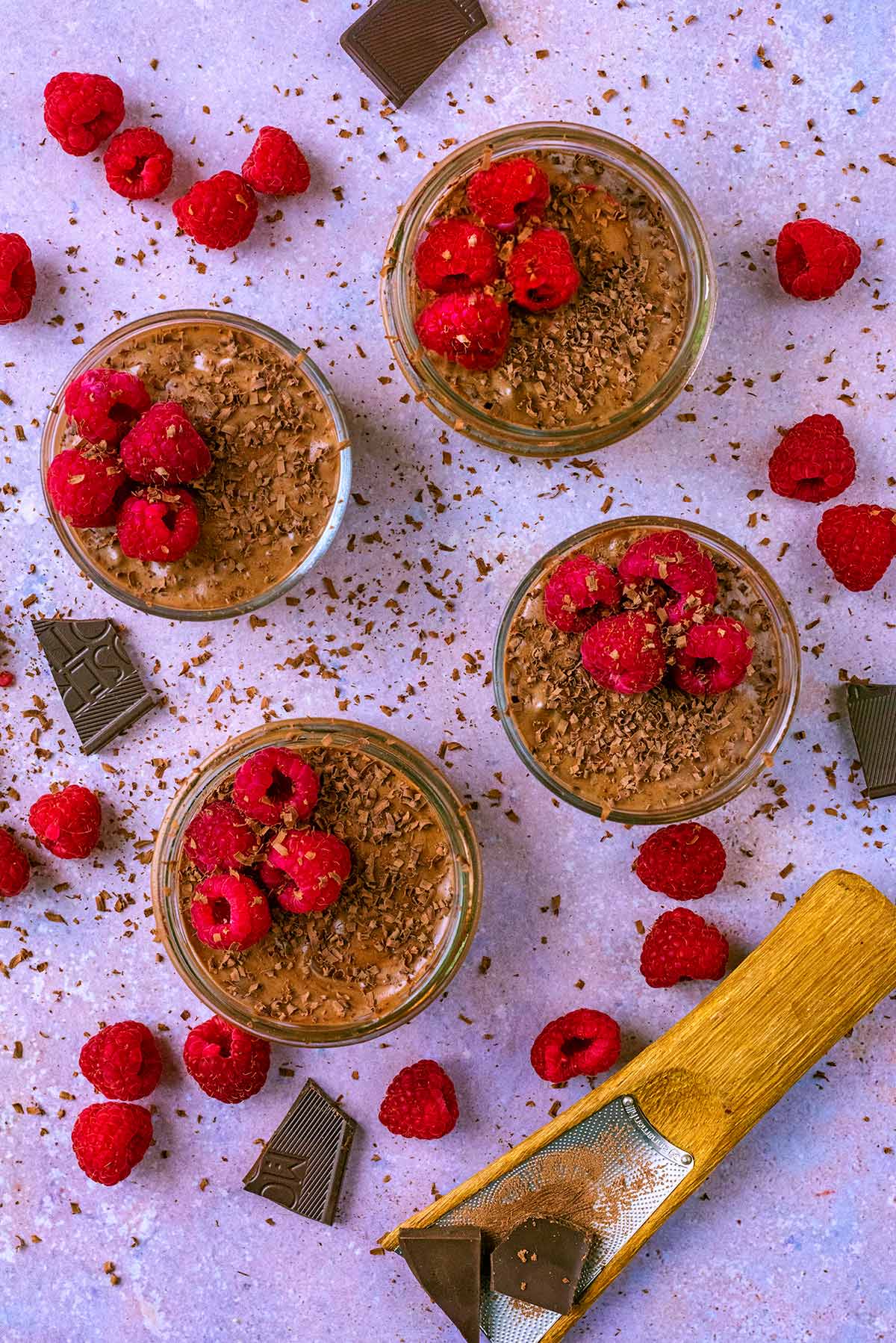 Four pots of chocolate mousse each topped with four raspberries.