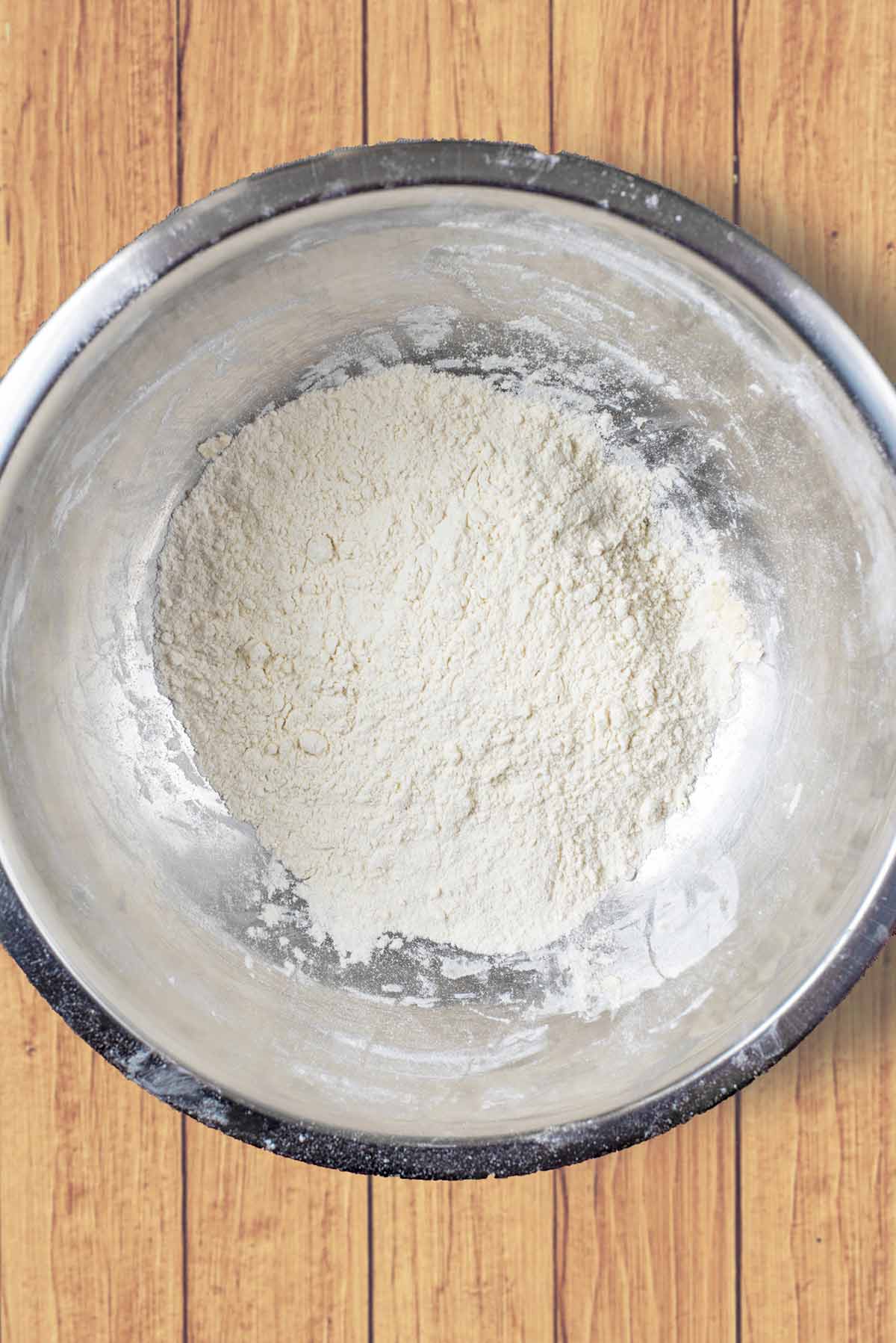 A stainless steel mixing bowl with flour in it.