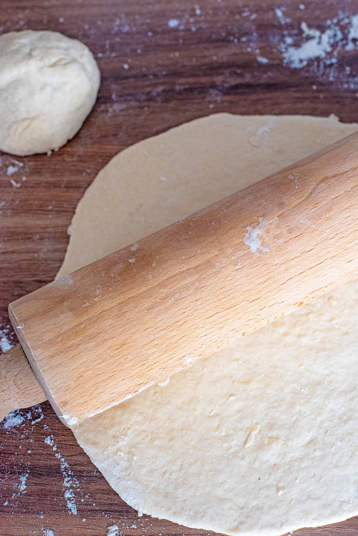 A ball of dough next to rolled out dough and a rolling pin.
