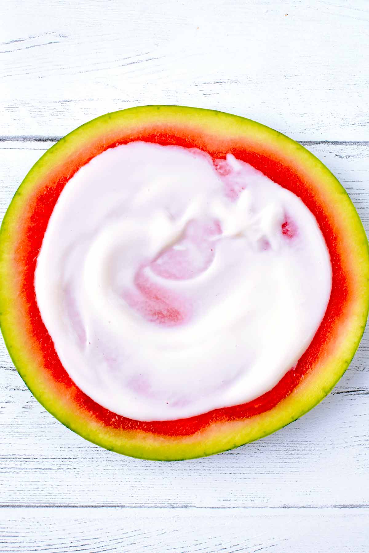 A round slice of watermelon with yogurt spread over it.