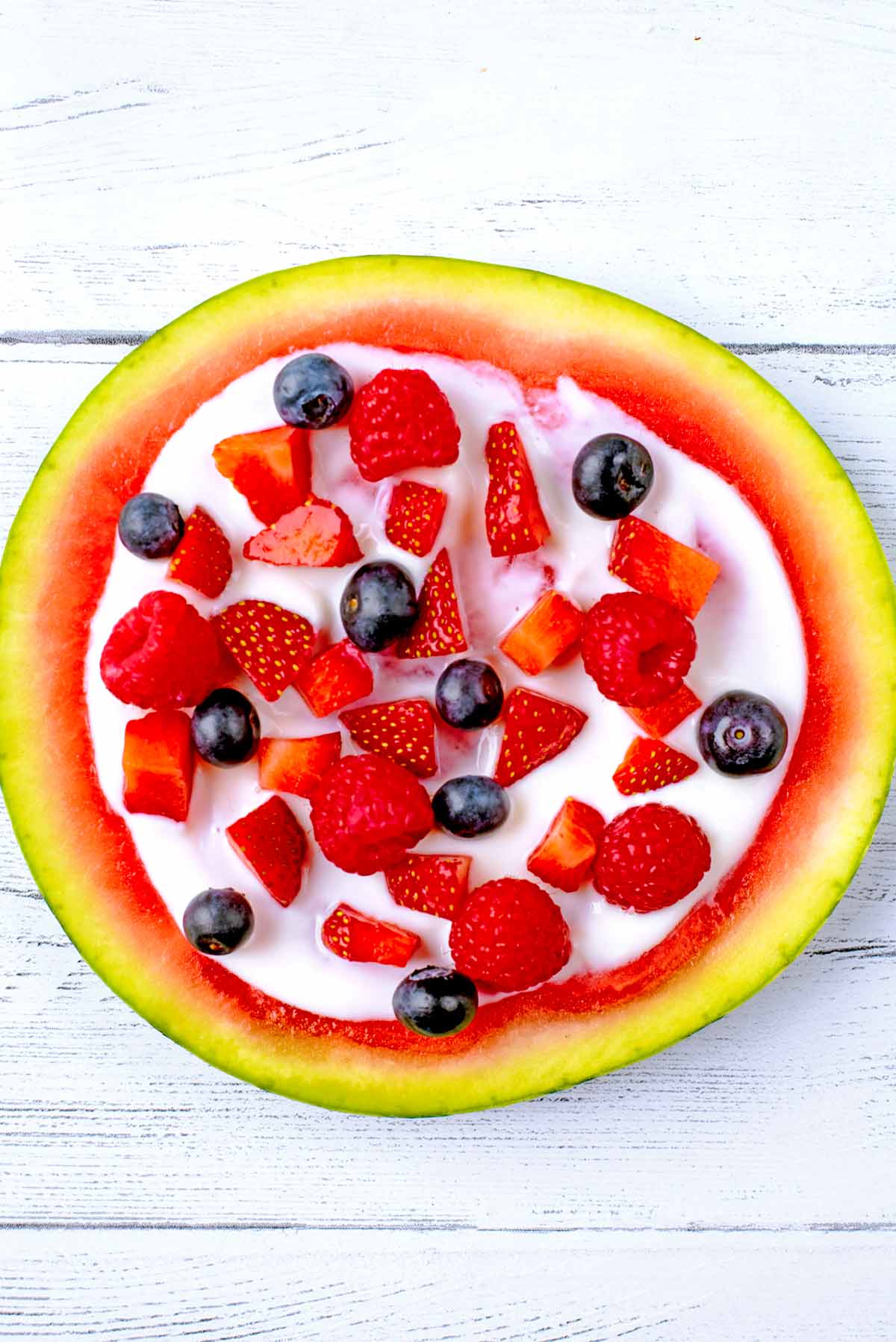 A round watermelon slice topped with yogurt and berries.