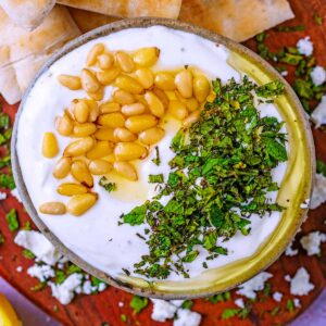 Whipped feta in a bowl topped with mint leaves and pine nuts.