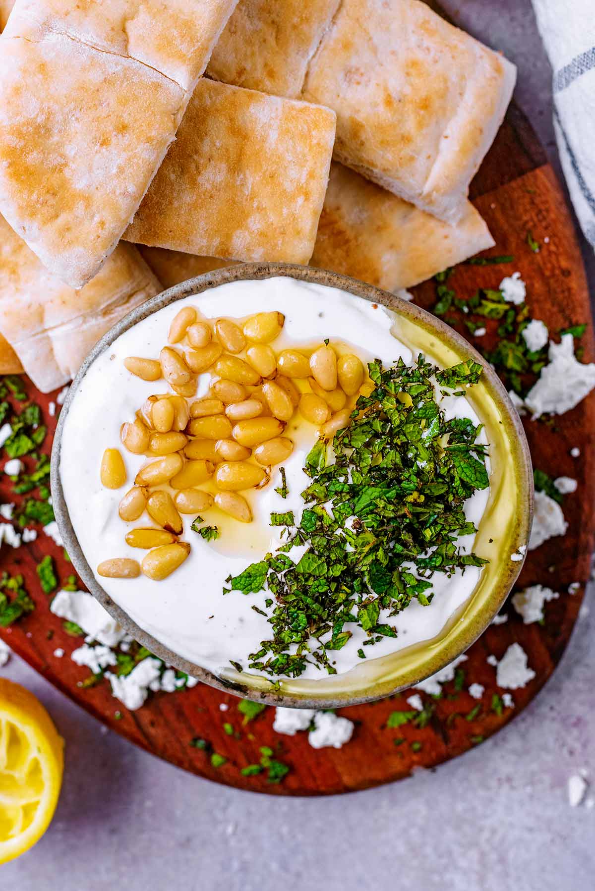 A bowl of feta dip on a board with sliced pita bread.