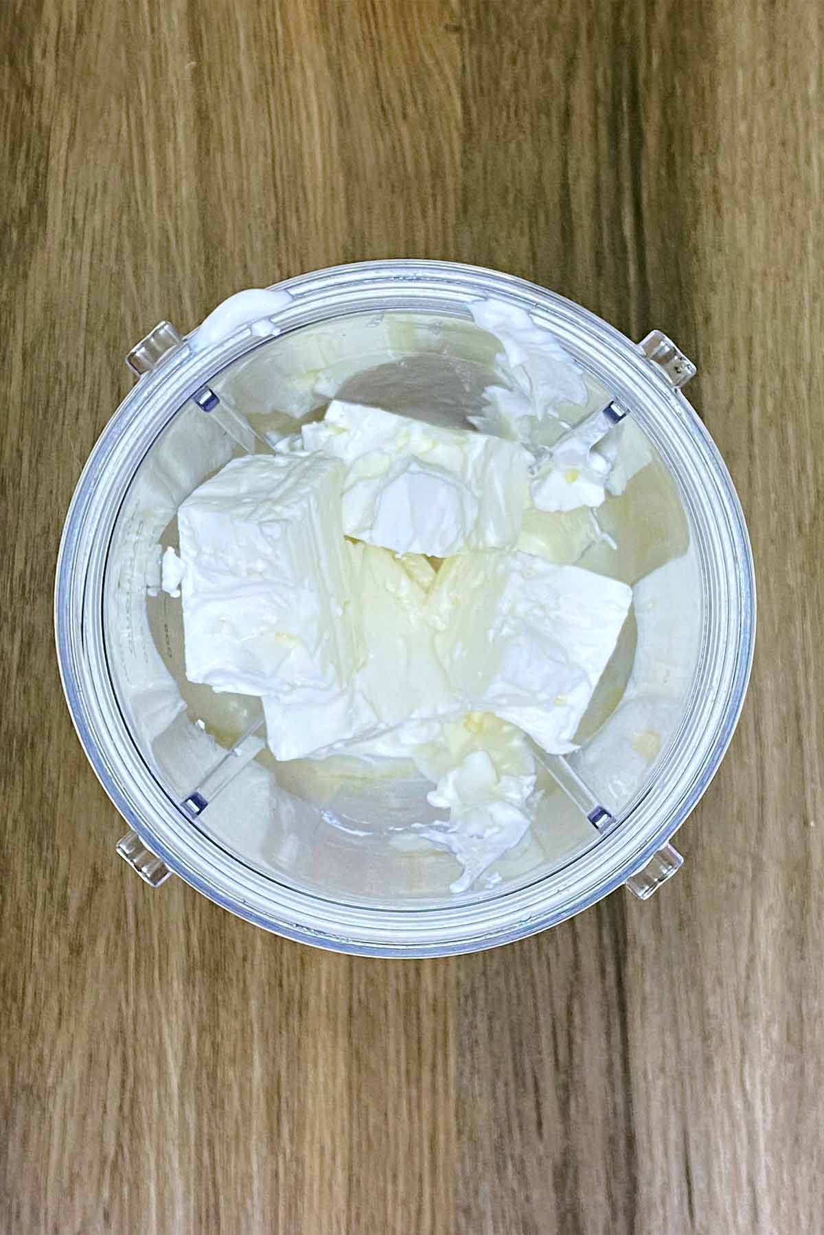 A blender jug with yogurt and chunks of feta in it.