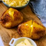 Two air fryer jacket potatoes on a wooden board.