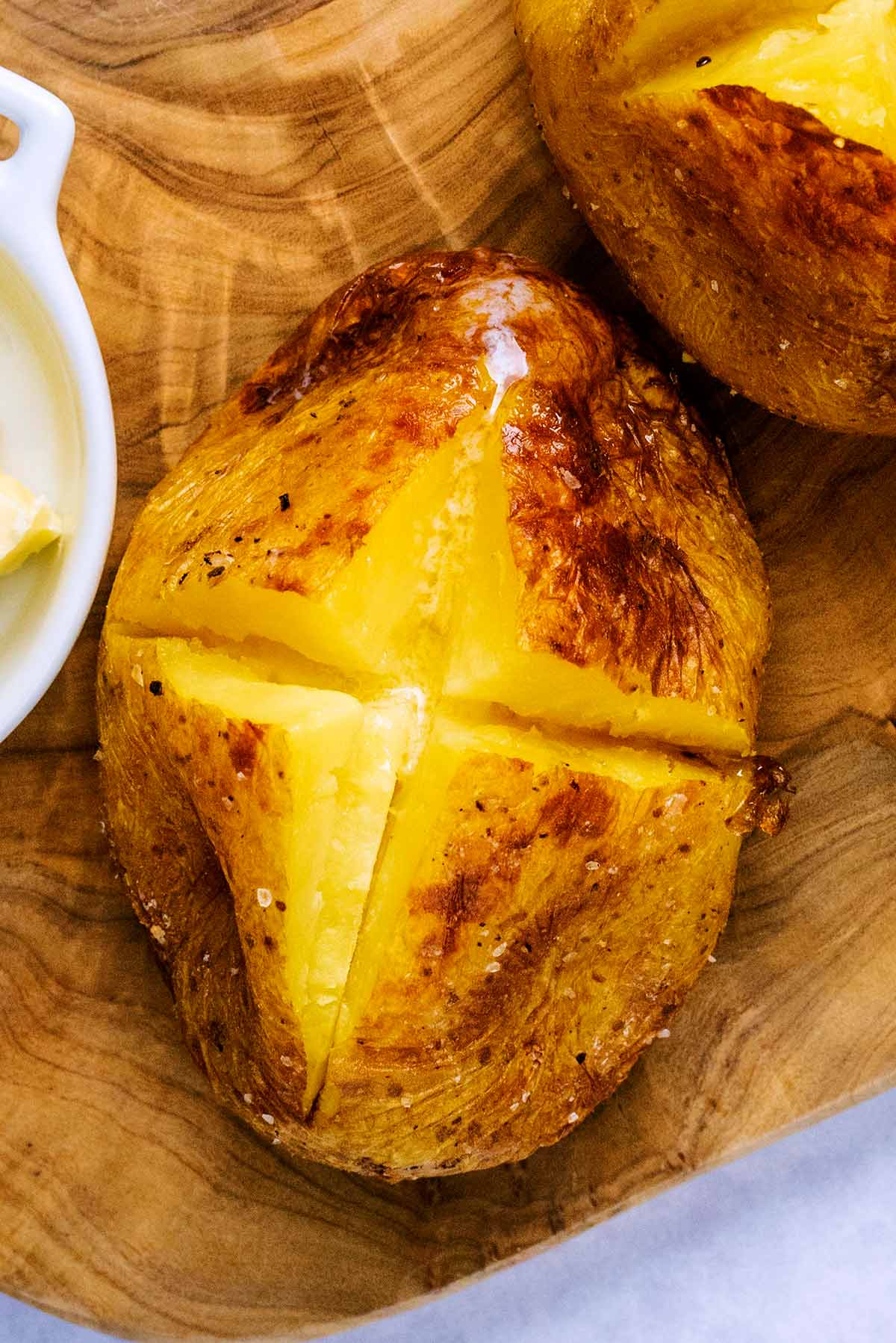 A baked potato cut open in a cross, with melted butter in it.