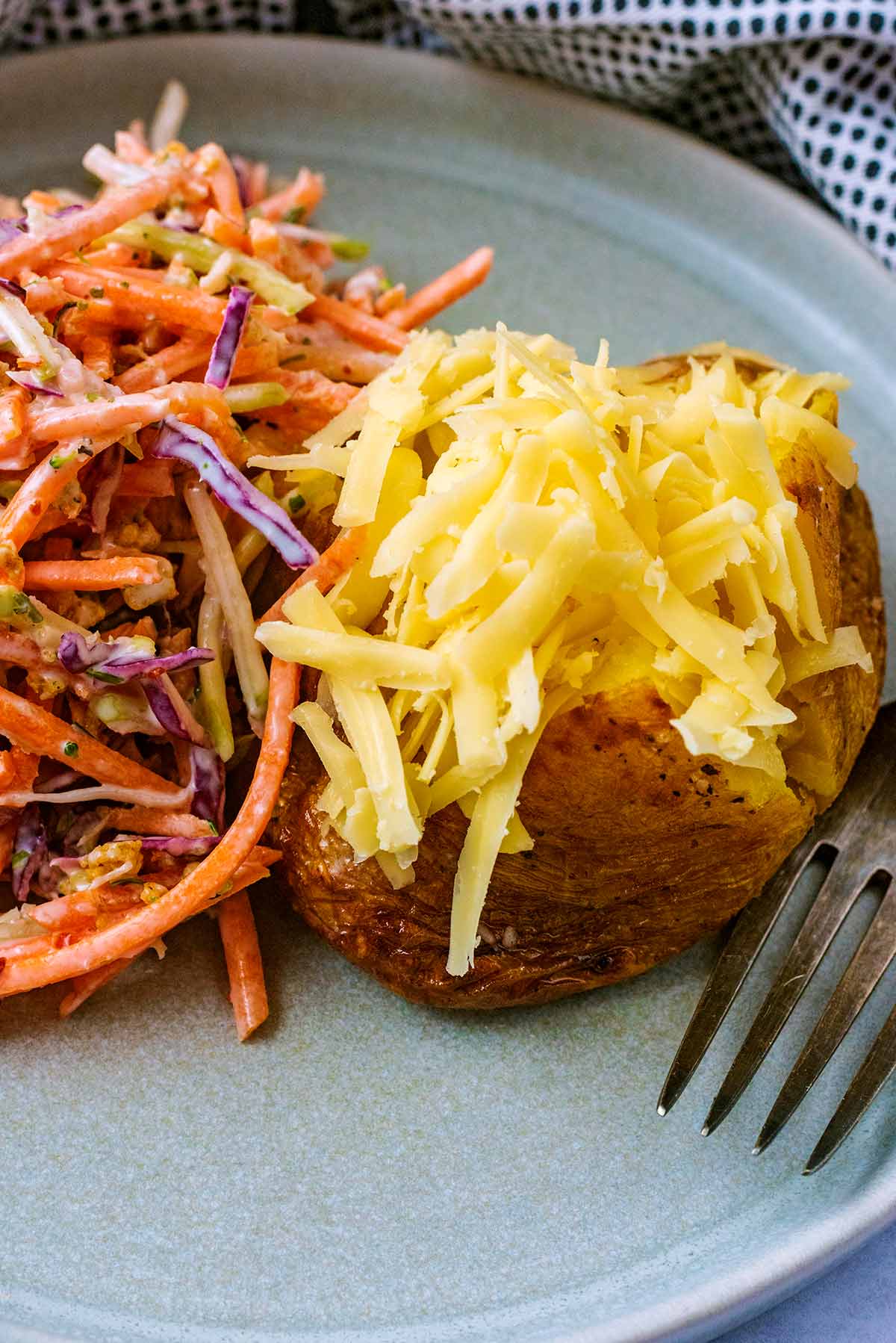 A cheese topped jacket potato on a plate next to some coleslaw.