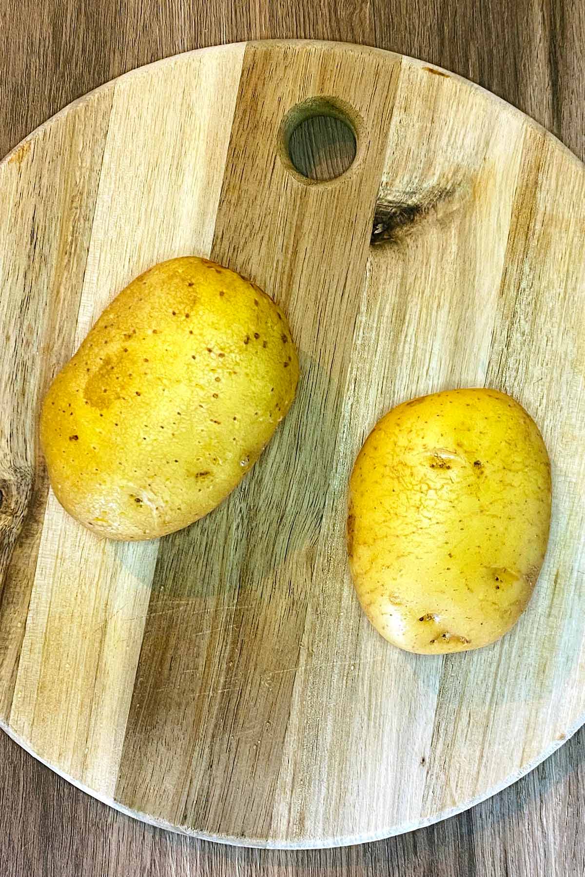 Two potatoes on a wooden board.