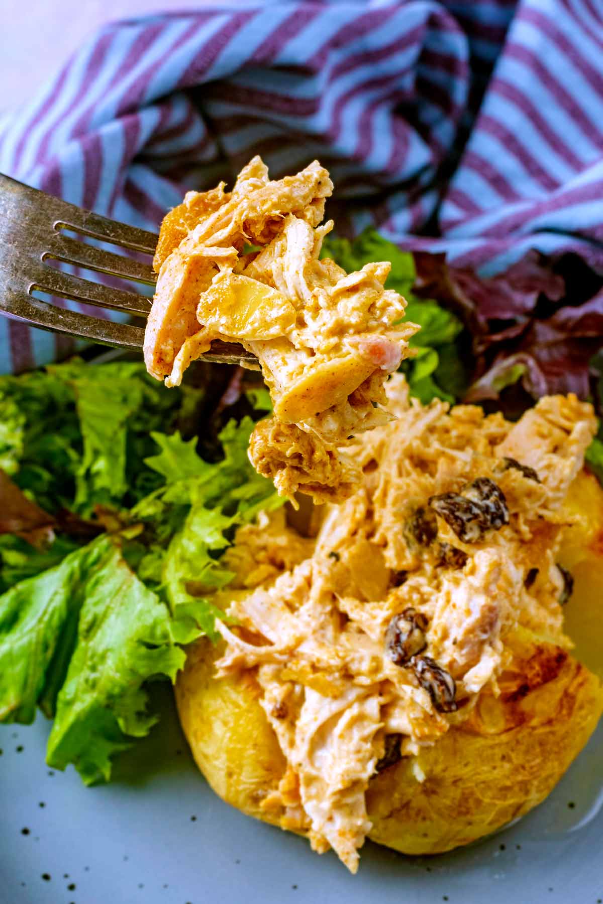 A fork picking come coronation chicken up from the top of a baked potato.