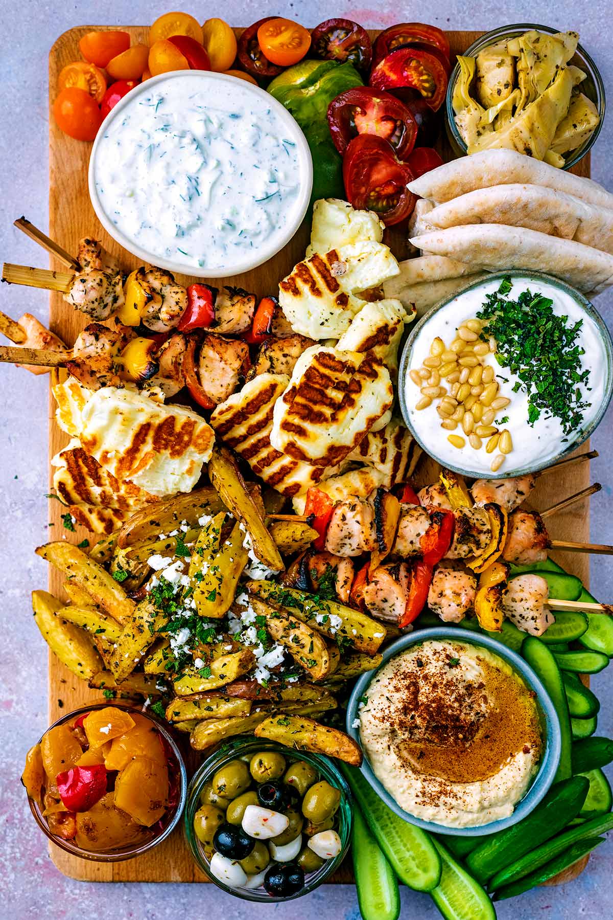 A meze platter made up of vegetables, chicken, bread, dips and cheese.