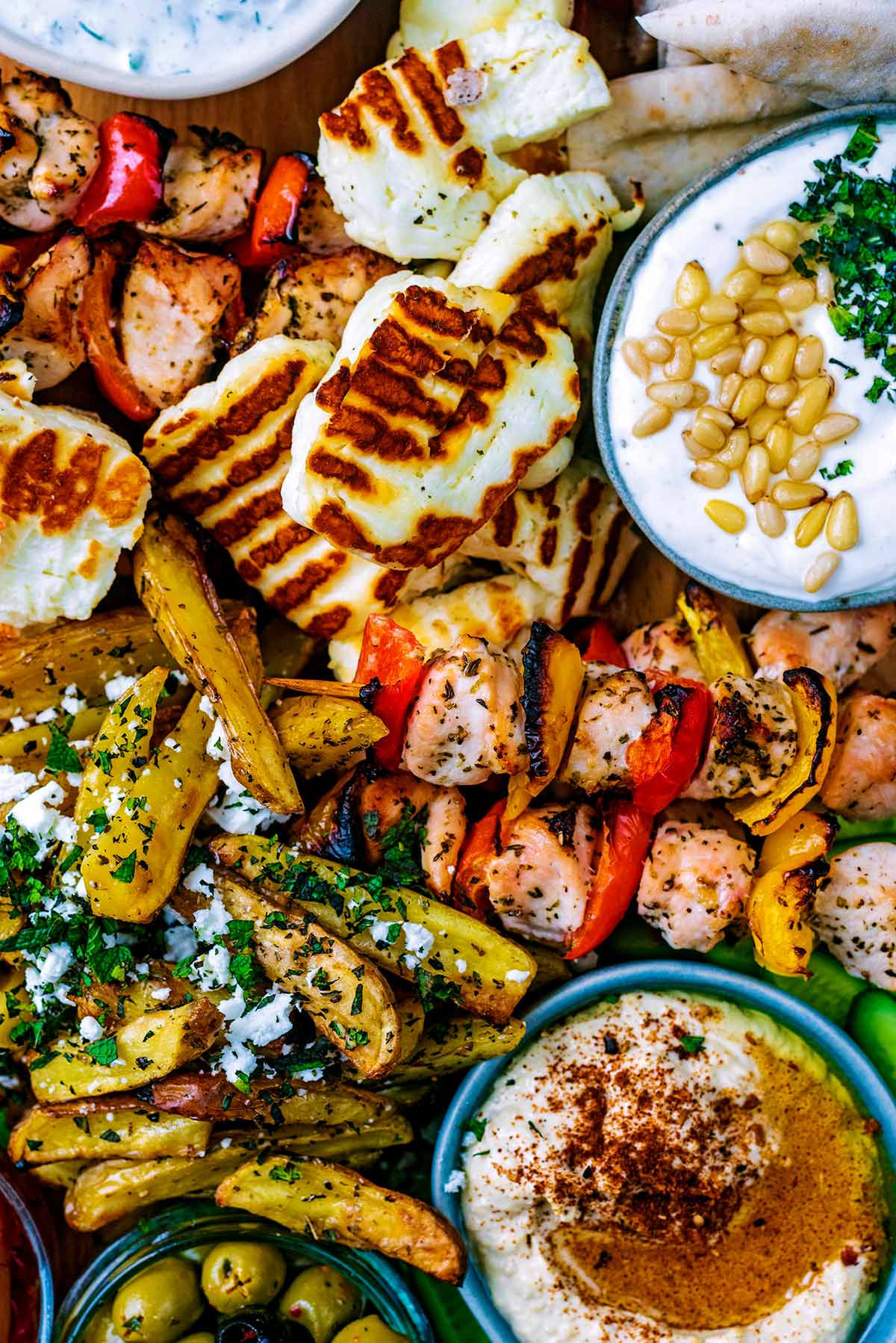 Sliced grilled halloumi, potato wedges, dips and chicken skewers arranged together on a board.
