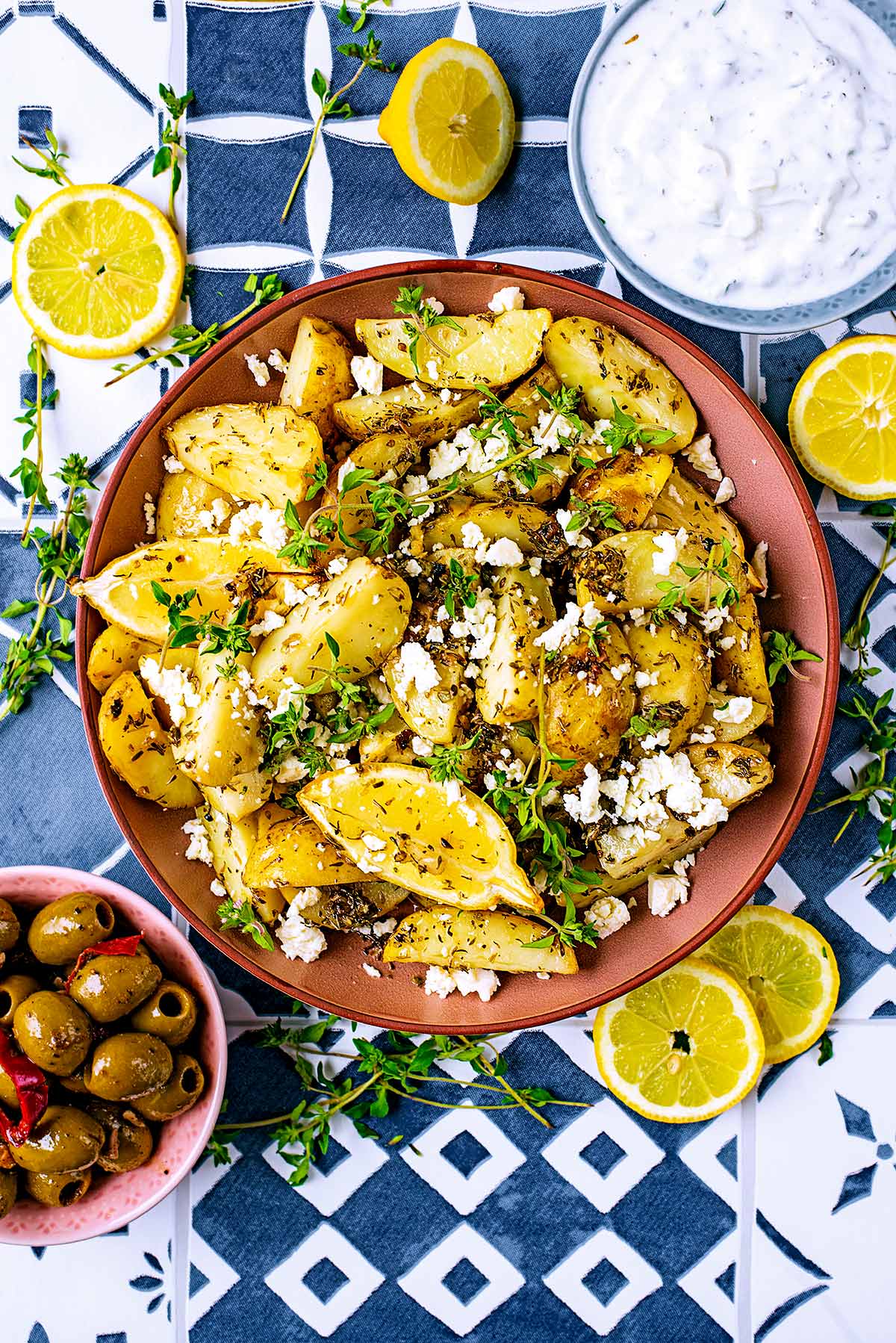 Greek Potatoes surrounded by tzatziki, olives and sliced lemons.