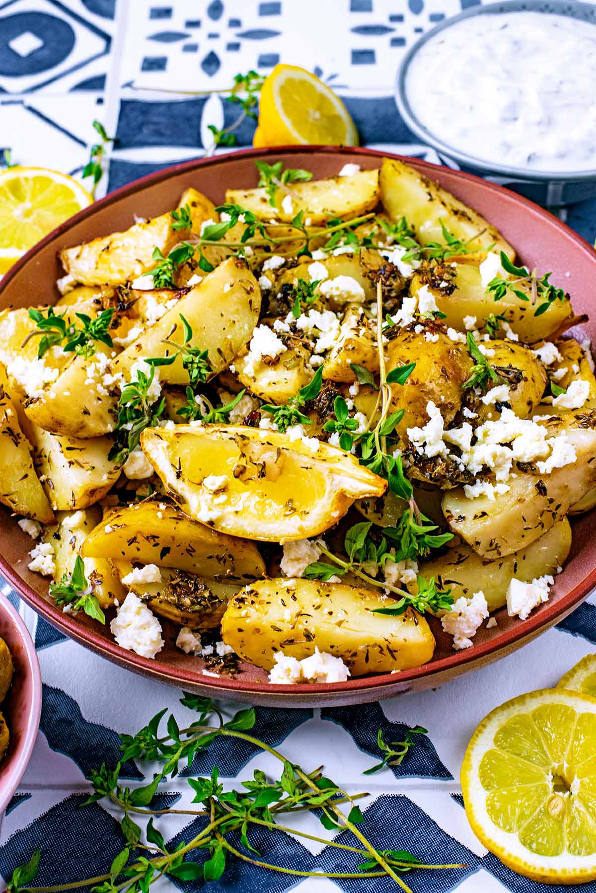 Greek Potatoes topped with lemon wedges, feta and sprigs of thyme.