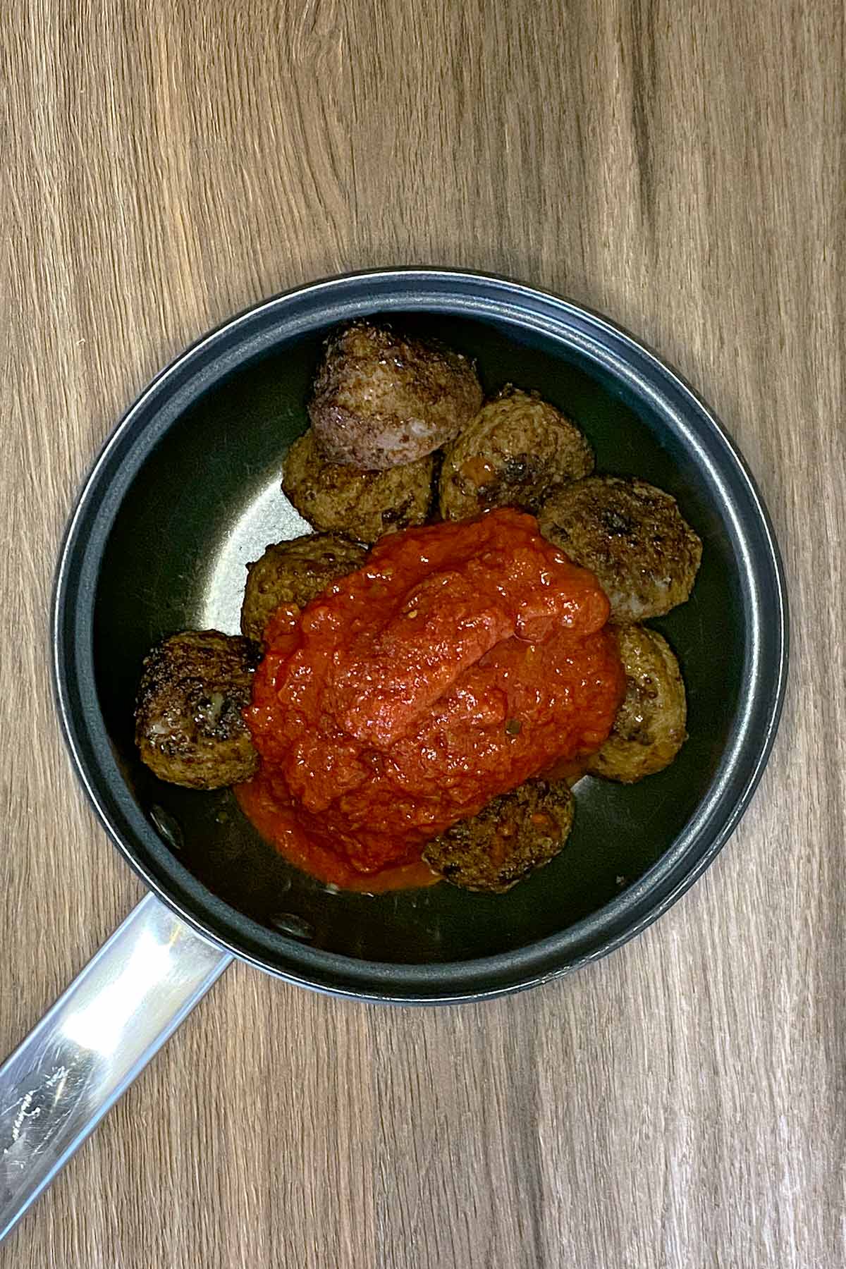 A saucepan containing meatballs and marinara sauce.