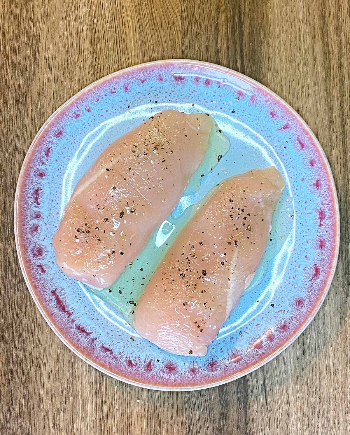 Two raw chicken breasts coated in oil and seasoning.