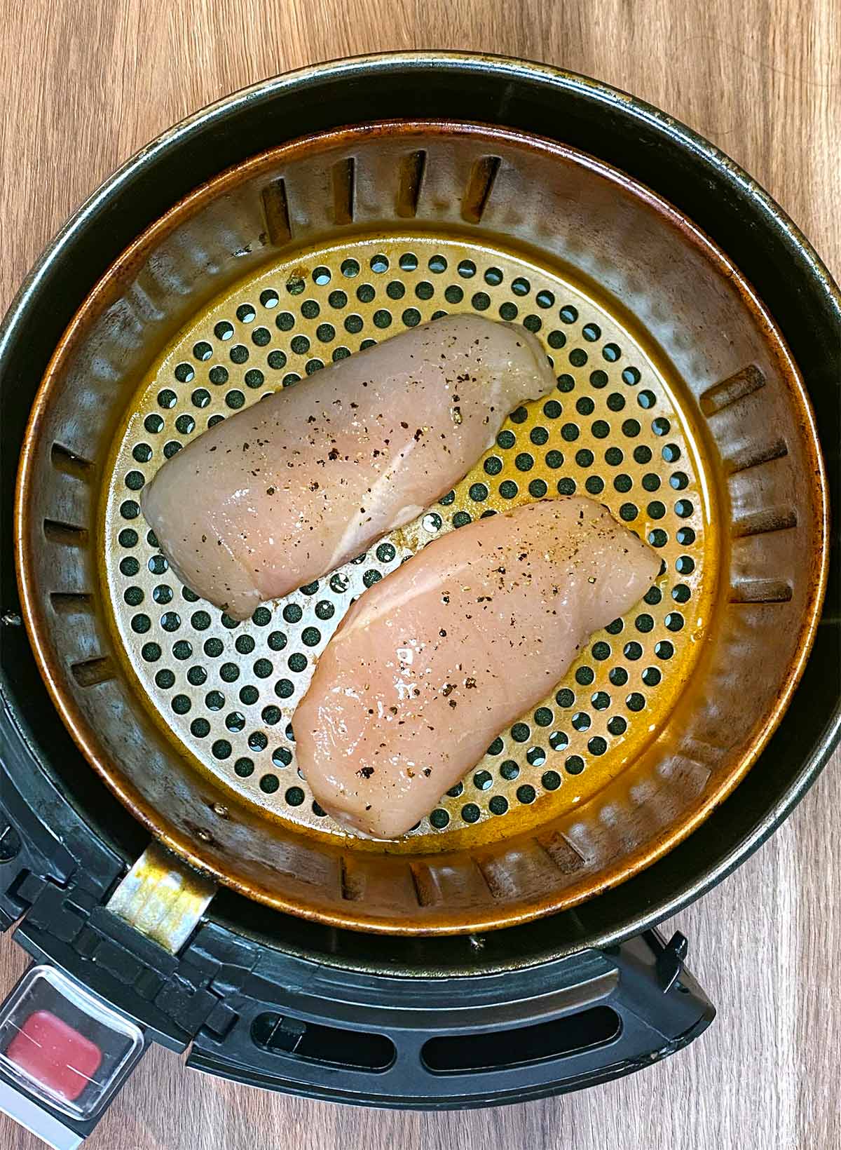 Two chicken breasts in an air fryer basket.