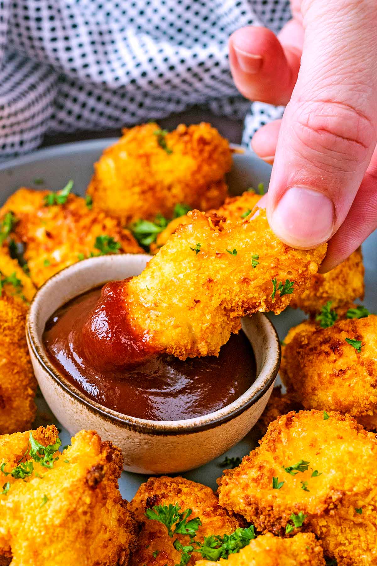 A chicken nugget being dipped into some barbecue sauce.