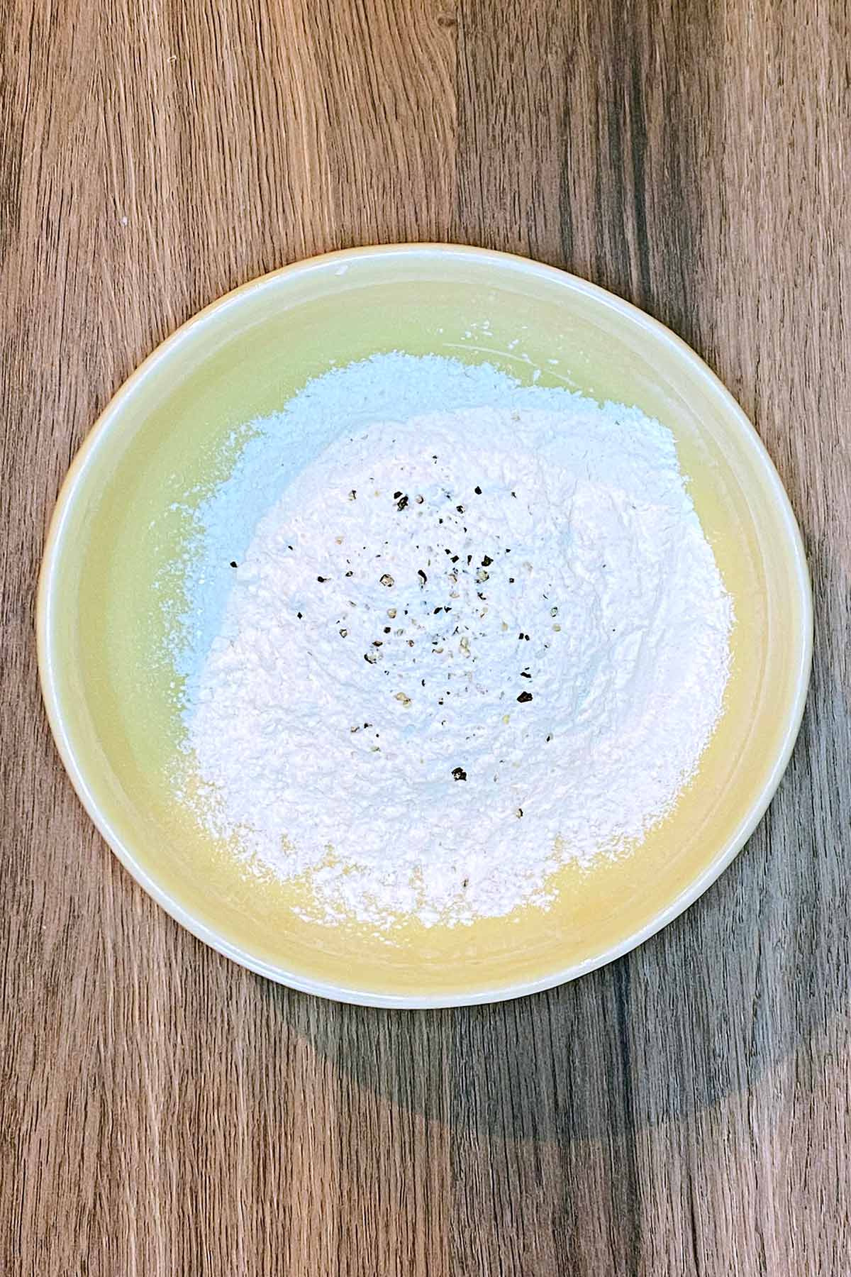 A bowl of flour with salt and pepper in it.