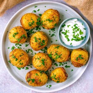 A plate of air fryer hasselback potatoes with a small pot of dip.