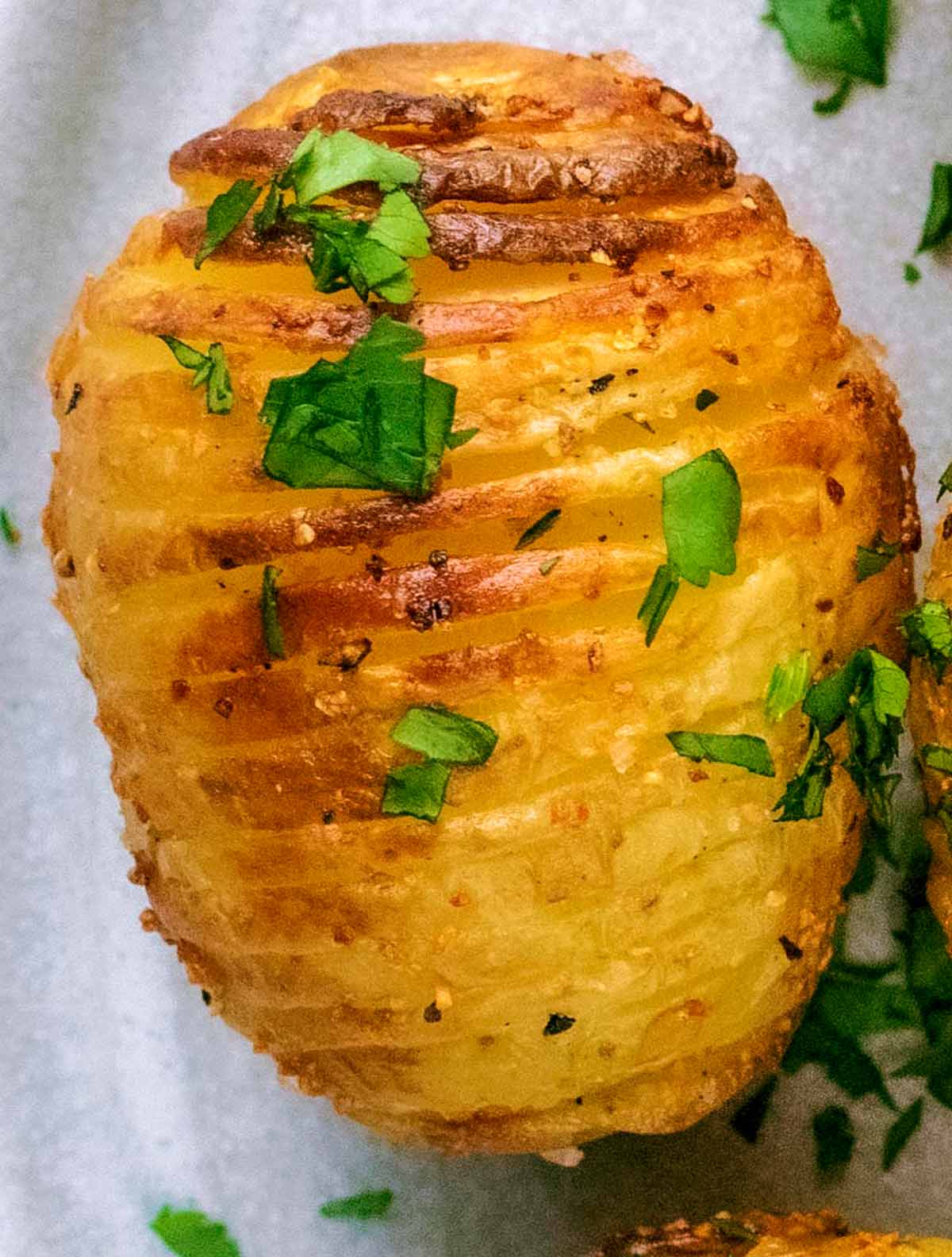 A cooked hasselback potato showing the slices topped with chopped herbs.