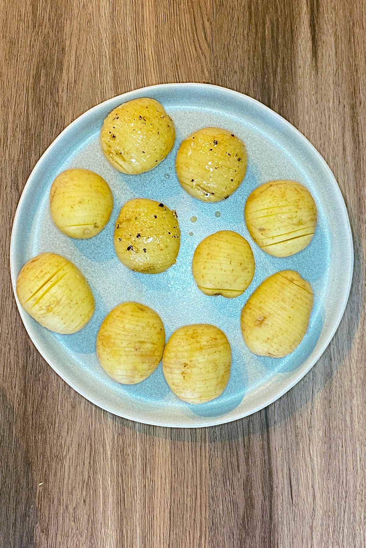 A plate of uncooked hasselback potatoes brushed with oil and seasoning.