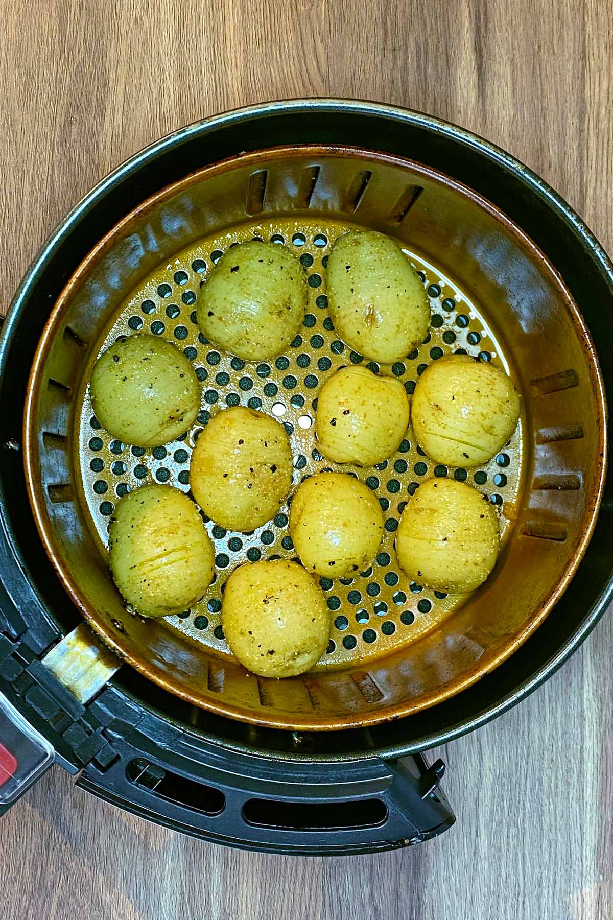 An air fryer basket containing uncooked hasselback potatoes.