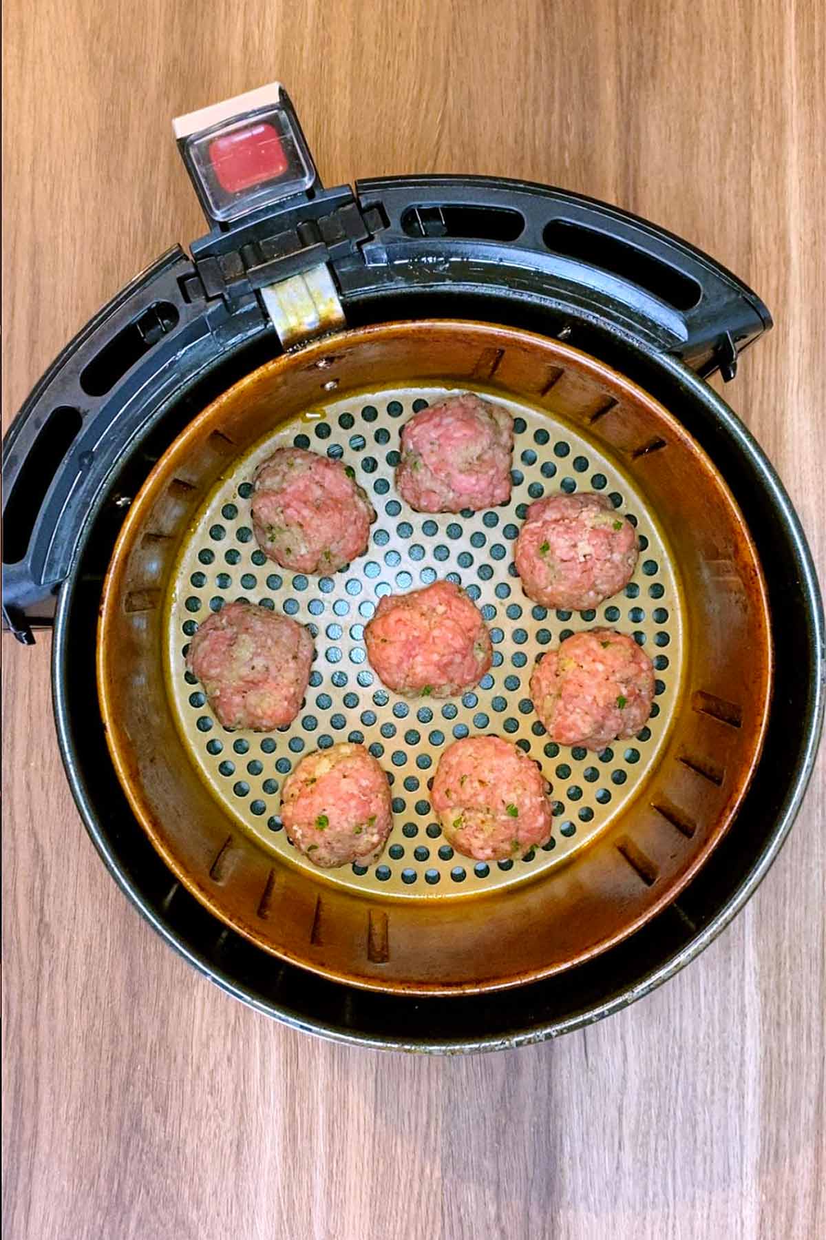 Eight uncooked meatballs in an air fryer basket.