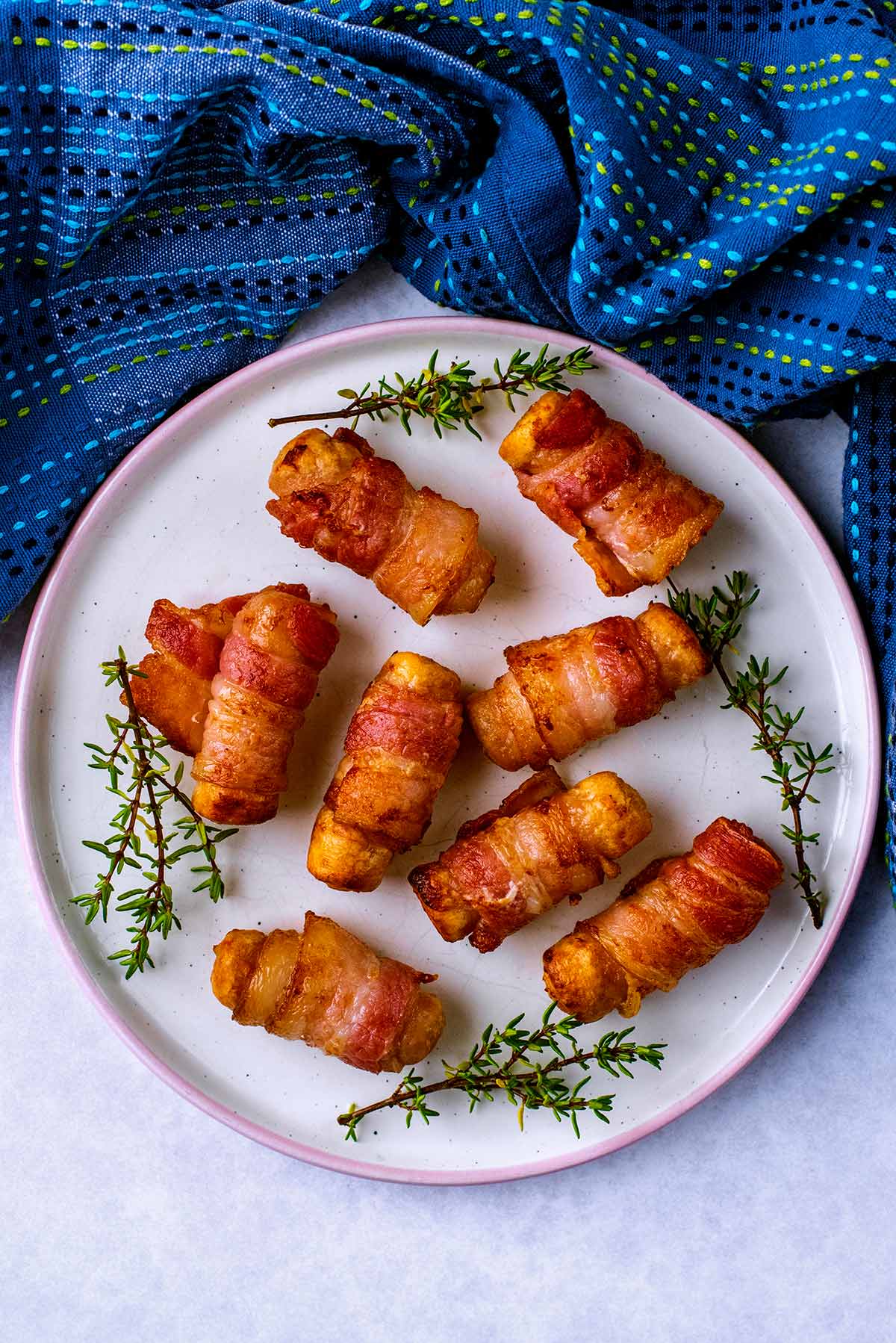 A plate of pigs in blankets with some sprigs of thyme.