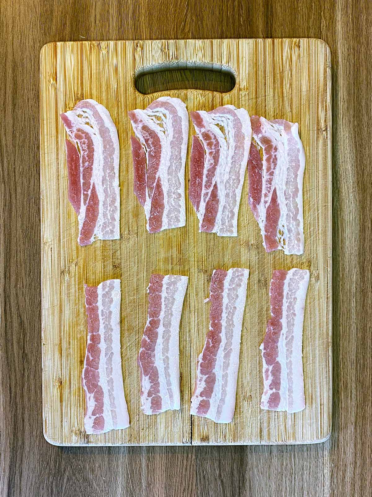 A chopping board with 4 rashers of bacon cut in half.