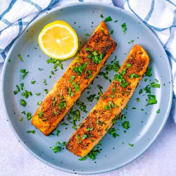 Two fillets of air fryer salmon on a plate with a lemon half.