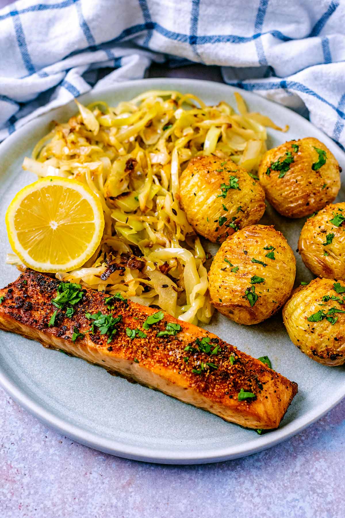 A plate of cooked salmon, cabbage and hasselback potatoes.