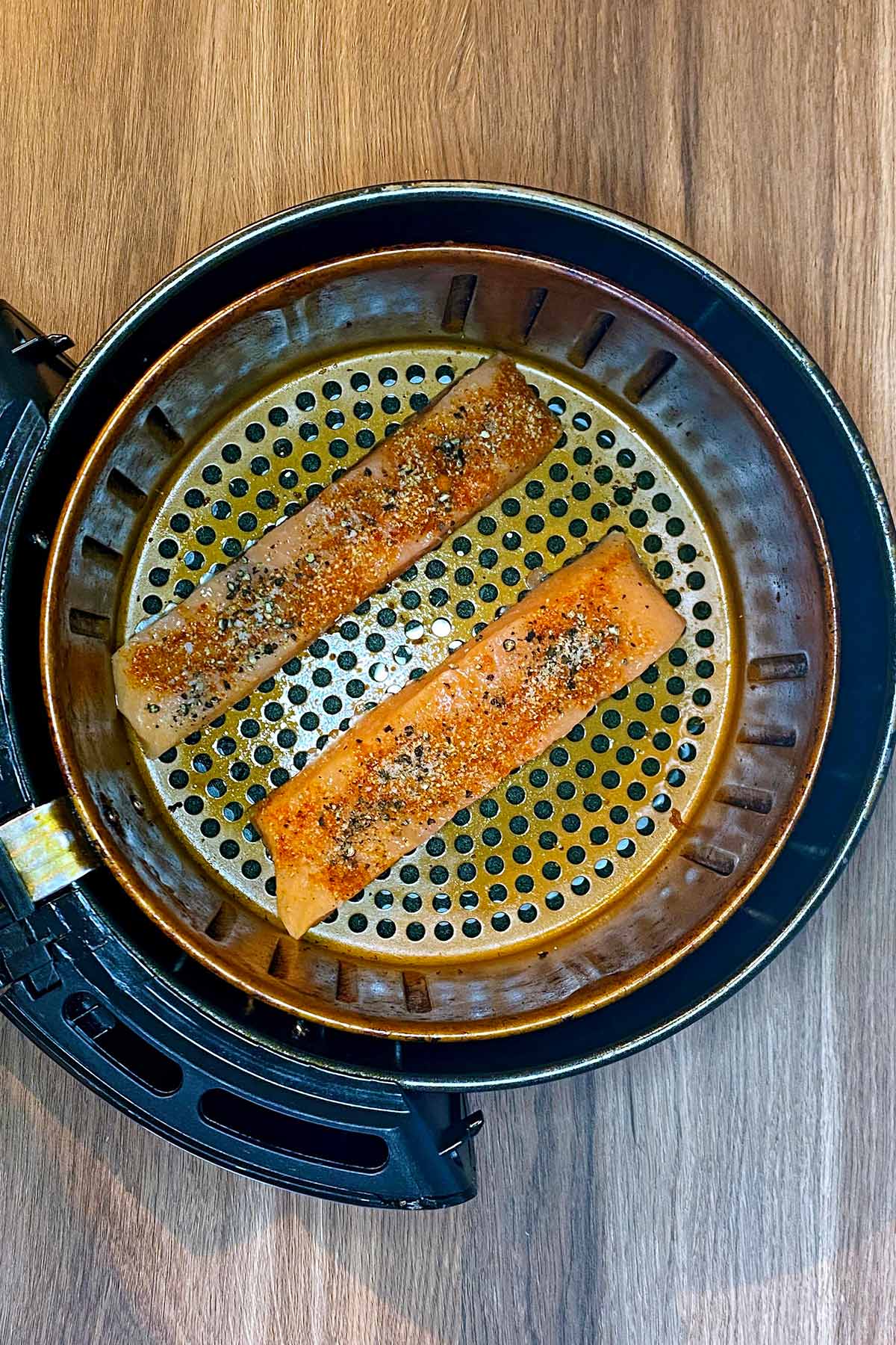 Salmon fillets in an air fryer basket.