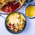 A bowl of apple and blackberry crumble topped with custard.