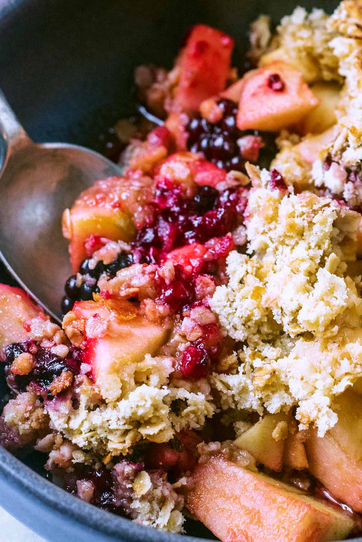 A spoon digging into a bowl of fruit crumble.