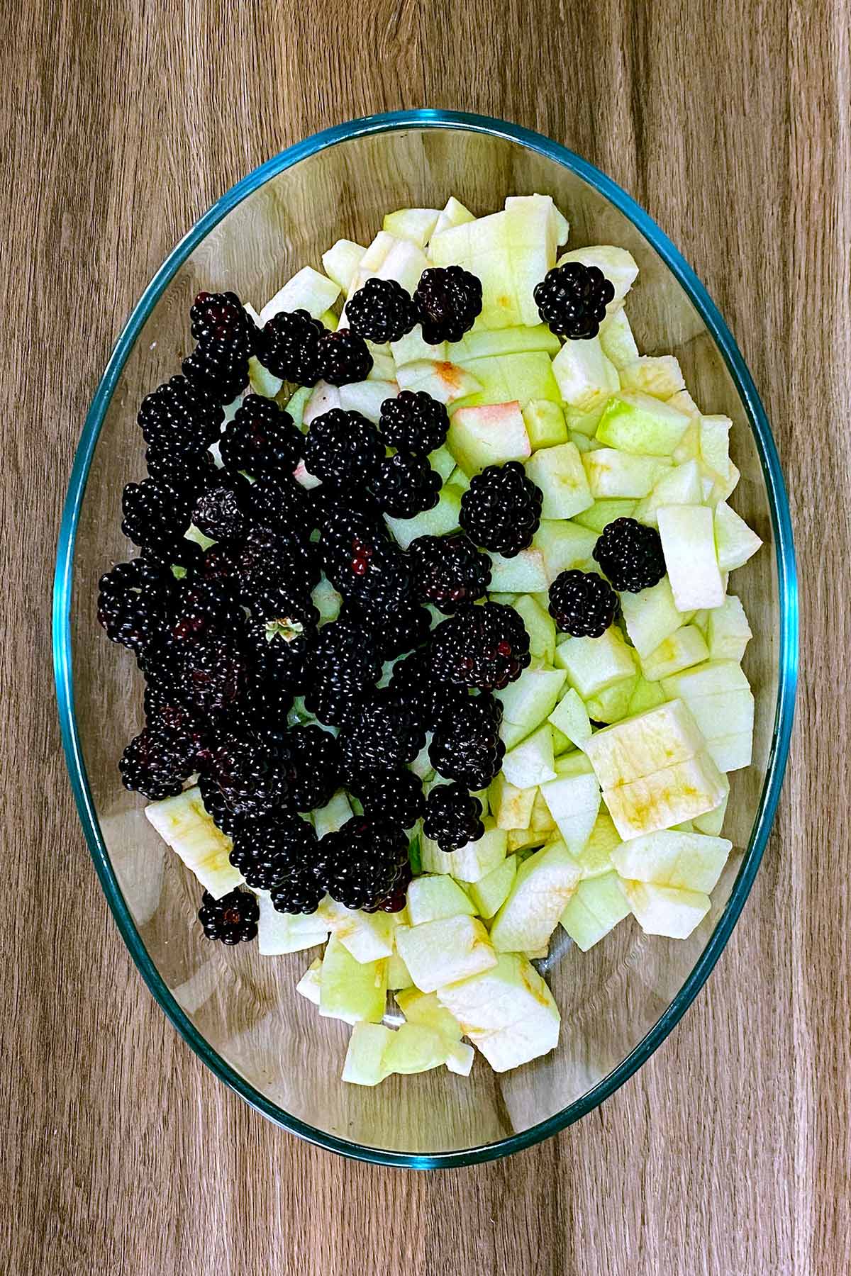 A large glass baking dish full of blackberries and chopped apples.