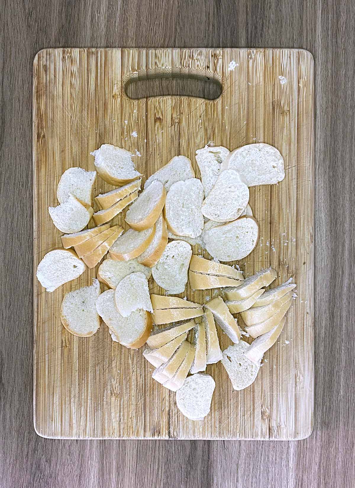 A wooden chopping board covered in disks of sliced bagel.