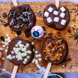 Four chocolate covered apple slices with various decorations.