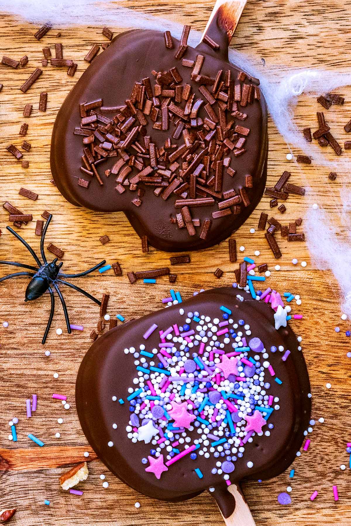 Two chocolate coated apple slices decorated with sprinkles.