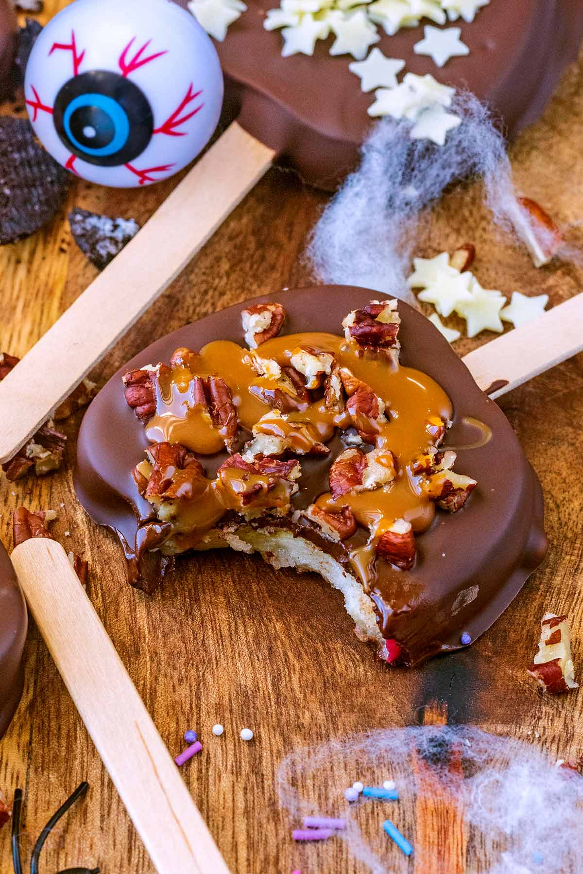 An apple slice covered in chocolate and decorated with nuts, with a bite taken out of it.