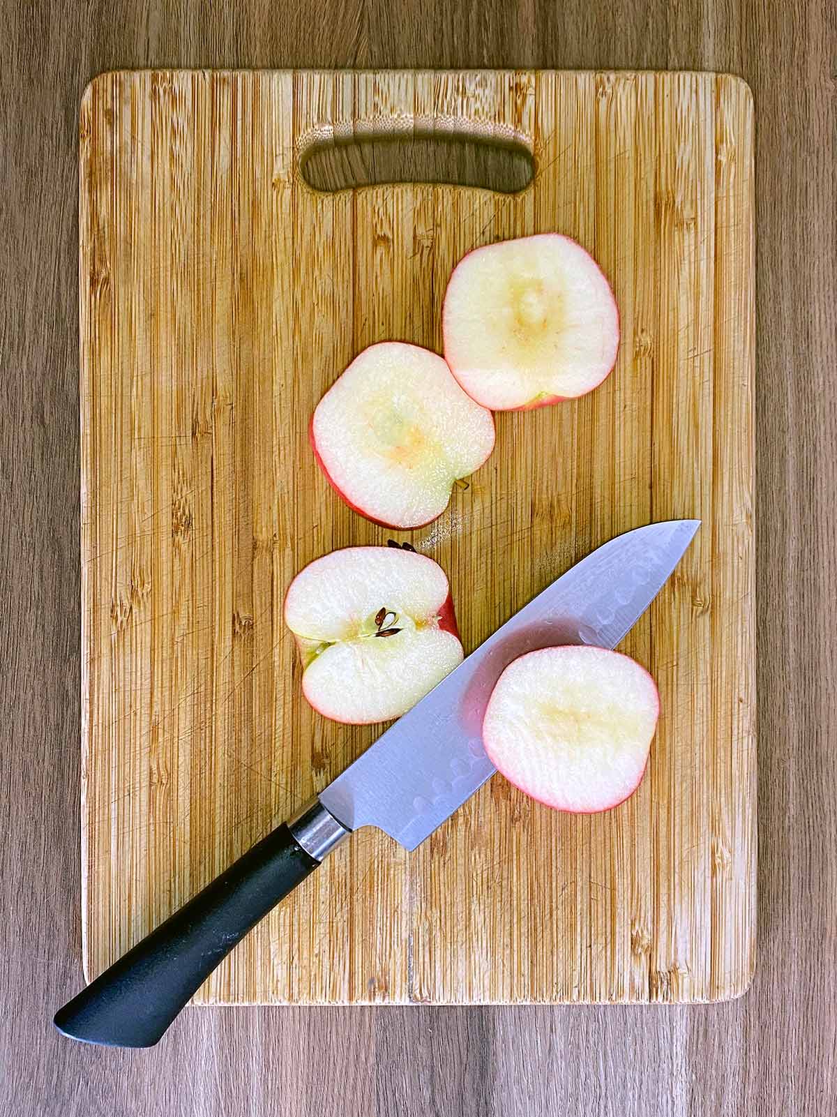 A wooden chopping board with a sliced apple and a chef's knife on it.