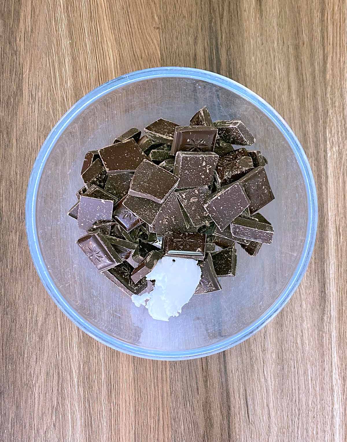 A glass bowl containing chunks of chocolate and coconut oil.