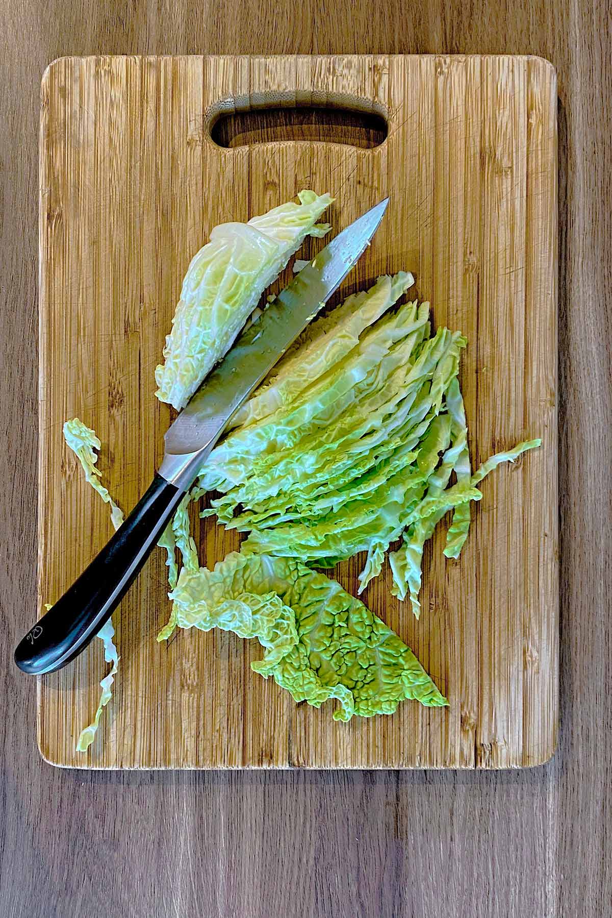 A chopping board with a shredded cabbage and a chef's knife on it.