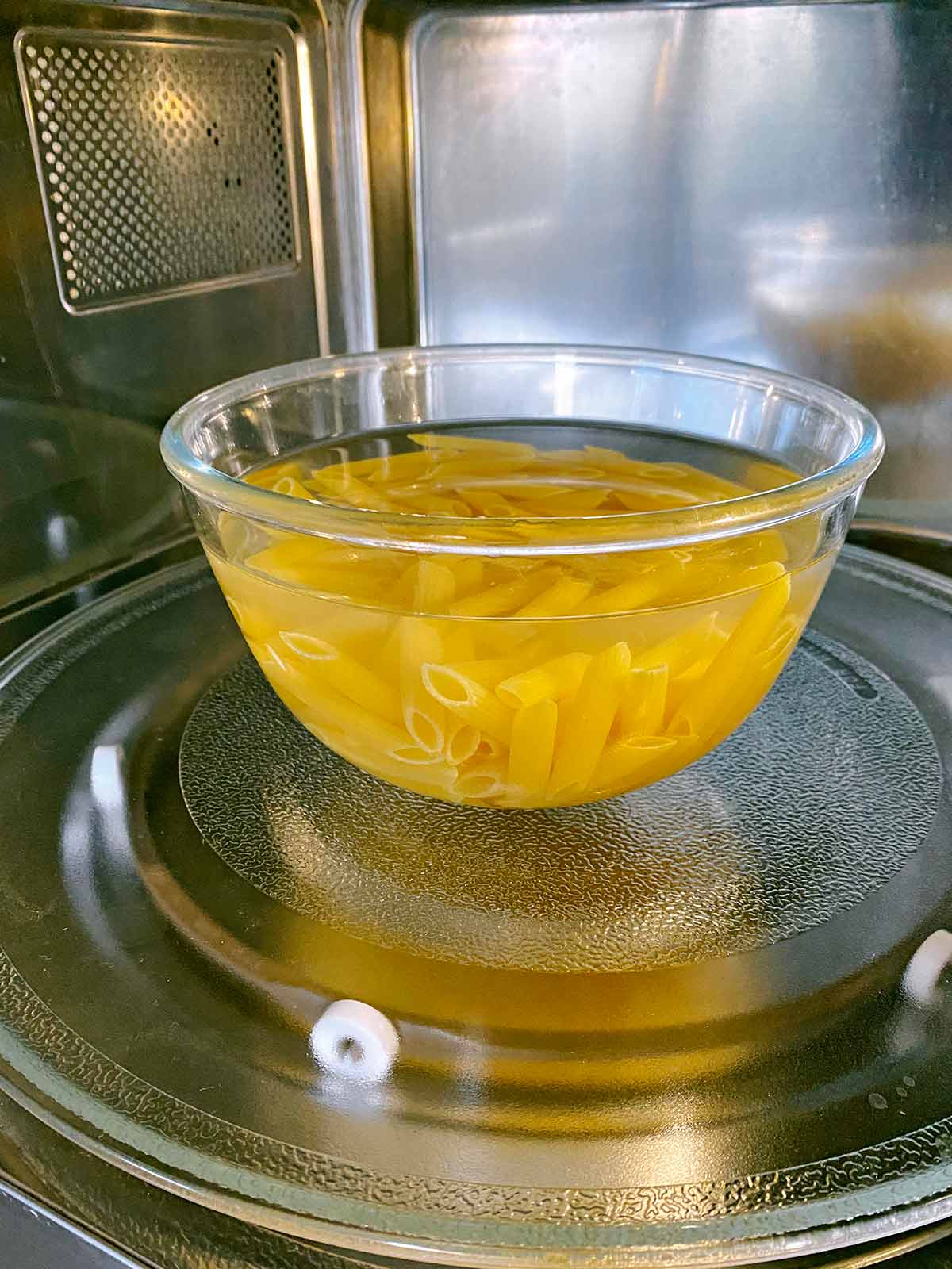 a bowl of water covered pasta inside a microwave.