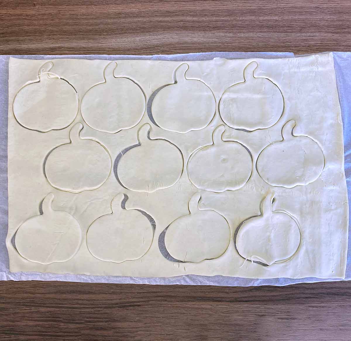 A sheet of pastry with pumpkin shapes cut into it.