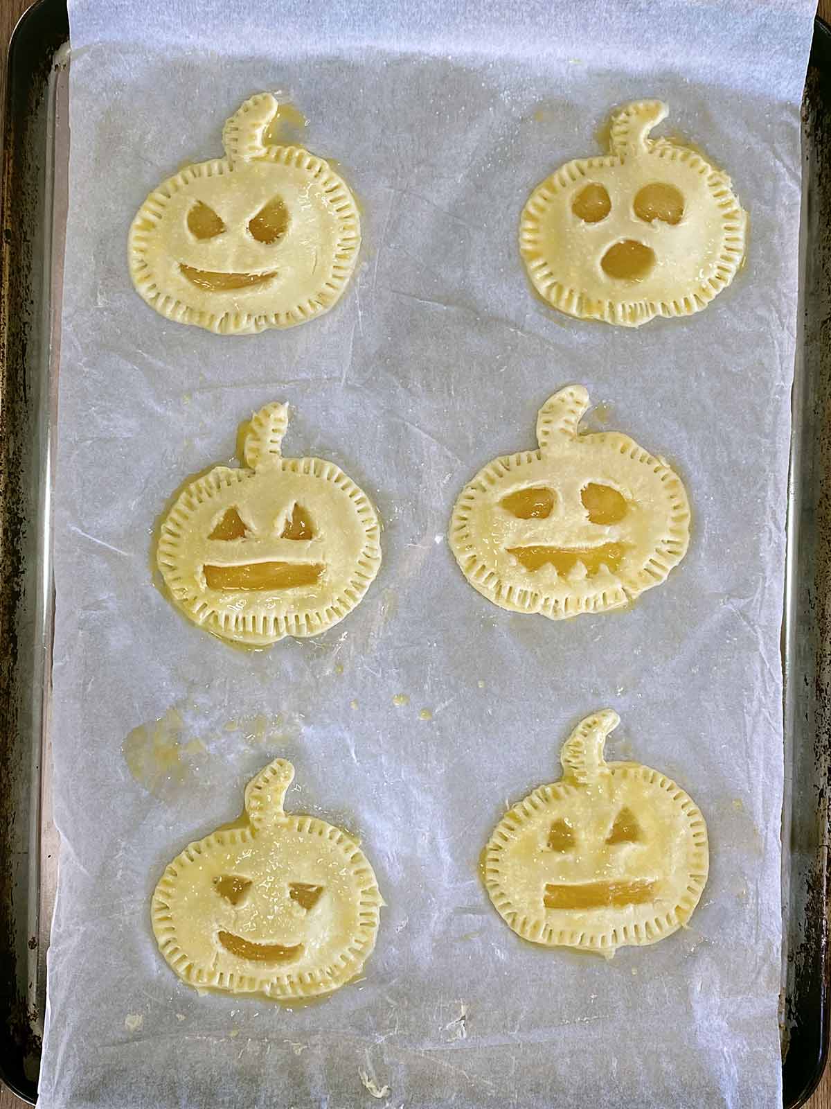 Six uncooked Halloween pies on a baking sheet.
